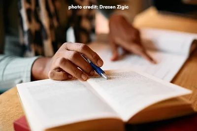 researcher's hand pointing to a paper, while looking something up on a book