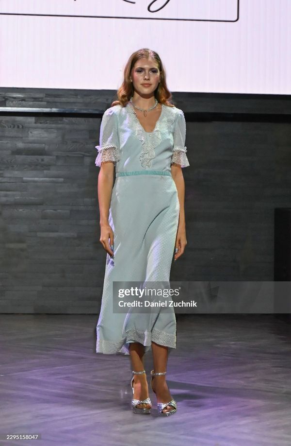 Female model walking runway in pastel dress and heels.