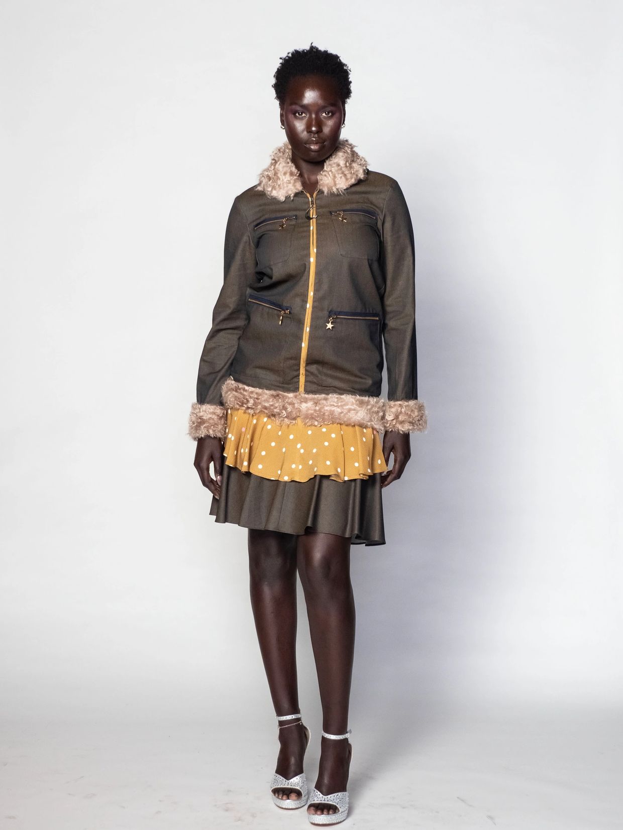 Model in layered outfit with fur-trimmed jacket and polka dot skirt.