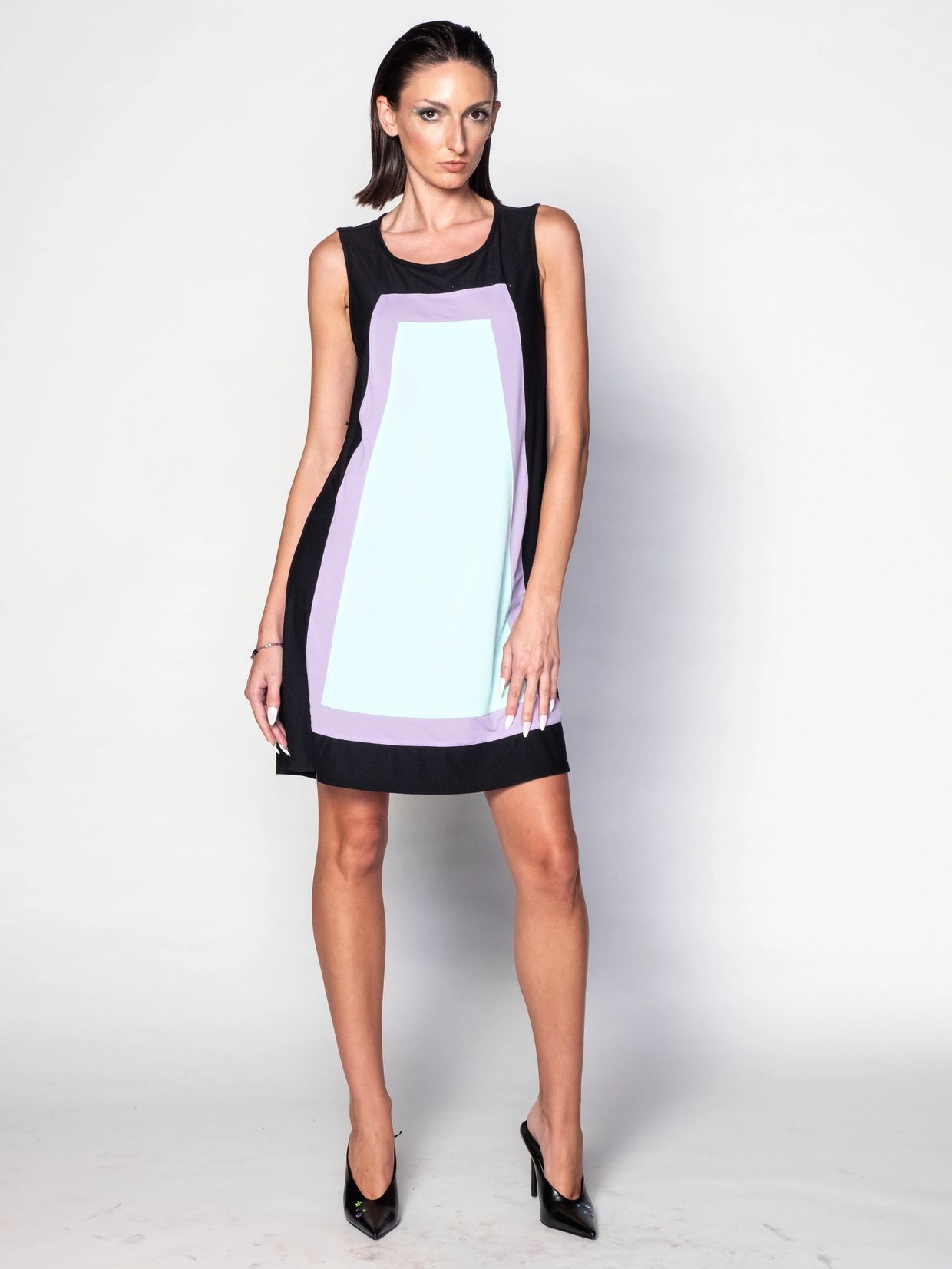 Woman in a sleeveless black dress with geometric patterns posing.