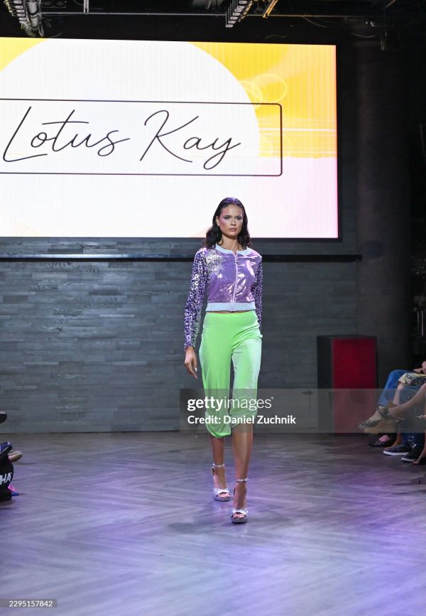 Model walking runway wearing purple sequin jacket and green pants.