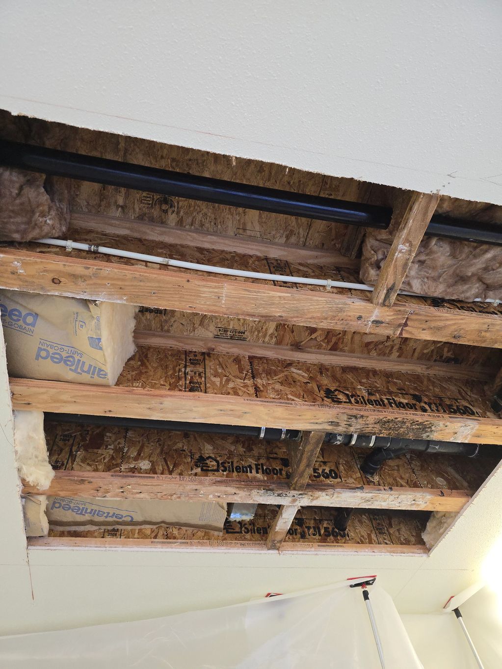Drywall removed on ceiling, plumbing and insulation visible.