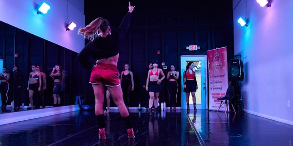 A dance instructor leads a group of women in a studio with colorful lighting.