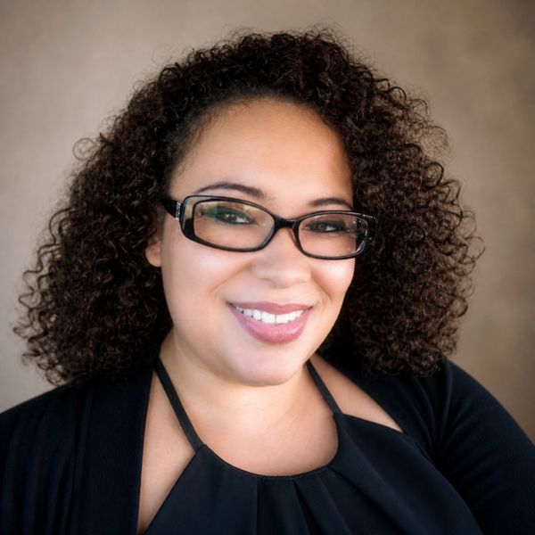 Smiling woman with curly hair and glasses in a black top.