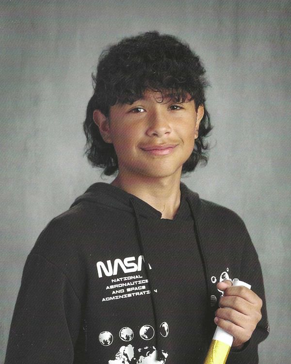 Teen with curly hair in a NASA hoodie holding a rolled paper, smiling.