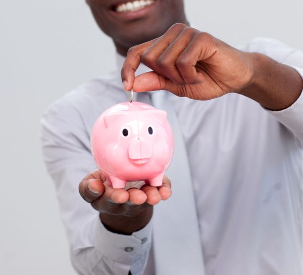 Homme déposant une pièce dans une tirelire en forme de cochon rose.