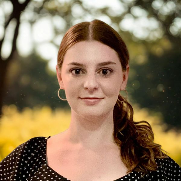 Young woman with brown hair and hoop earrings outdoors.
