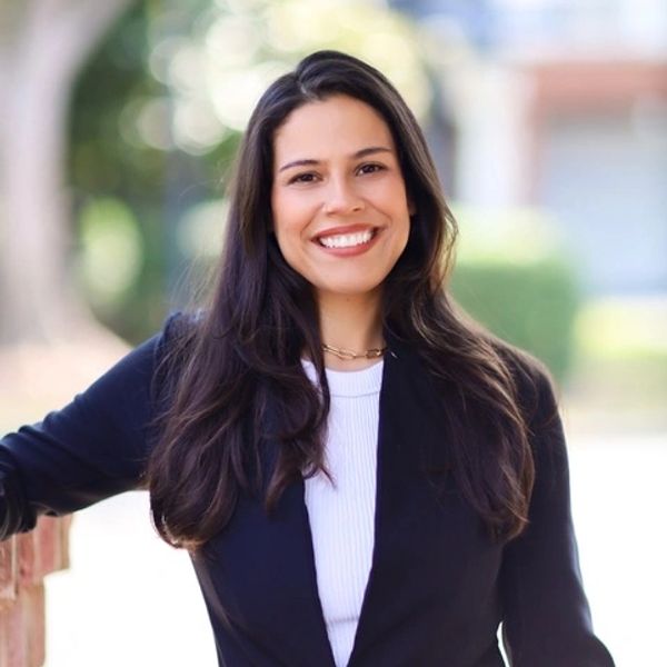 Smiling woman with long dark hair wearing a black blazer and white top.