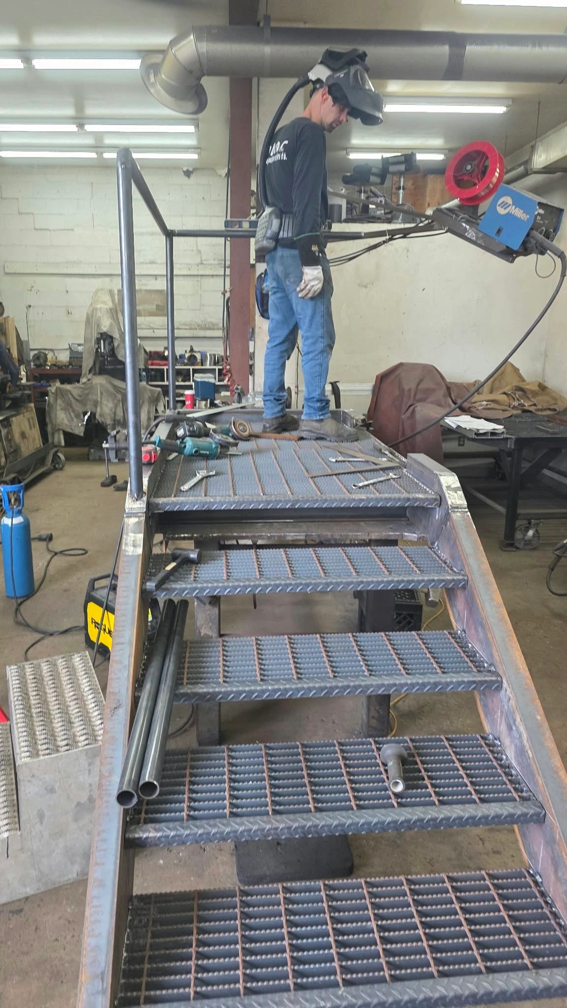 Man welding in industrial workshop with protective gear.