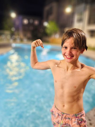 Boy flexing muscles by the pool at night.