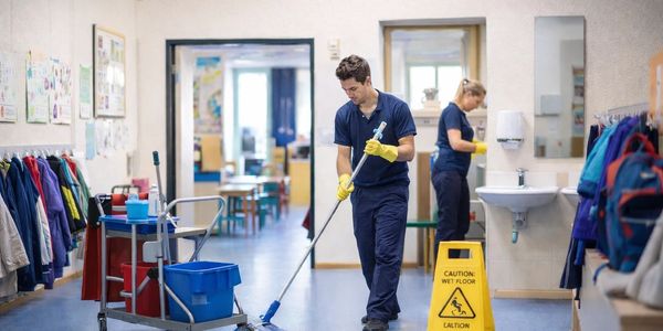 Two janitors cleaning a school hallway with caution sign.
