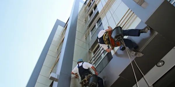 Two workers rappelling down a building cleaning windows with safety gear.