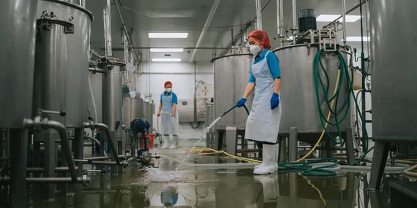 Workers cleaning a large stainless steel industrial facility floor with hoses.