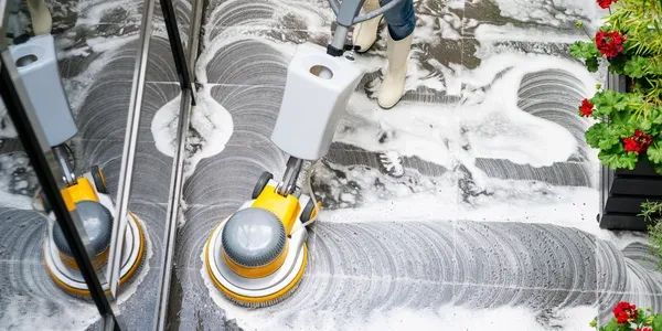 Person cleaning floor with a rotary scrubber and foam detergent.