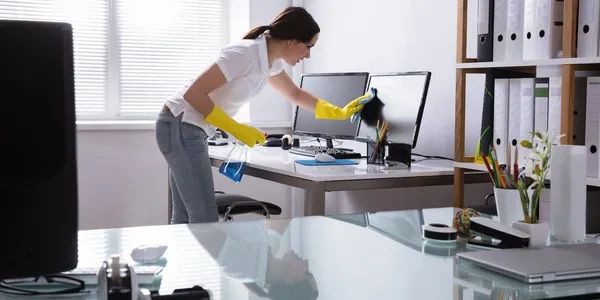 Woman cleaning computer screens in a bright office.