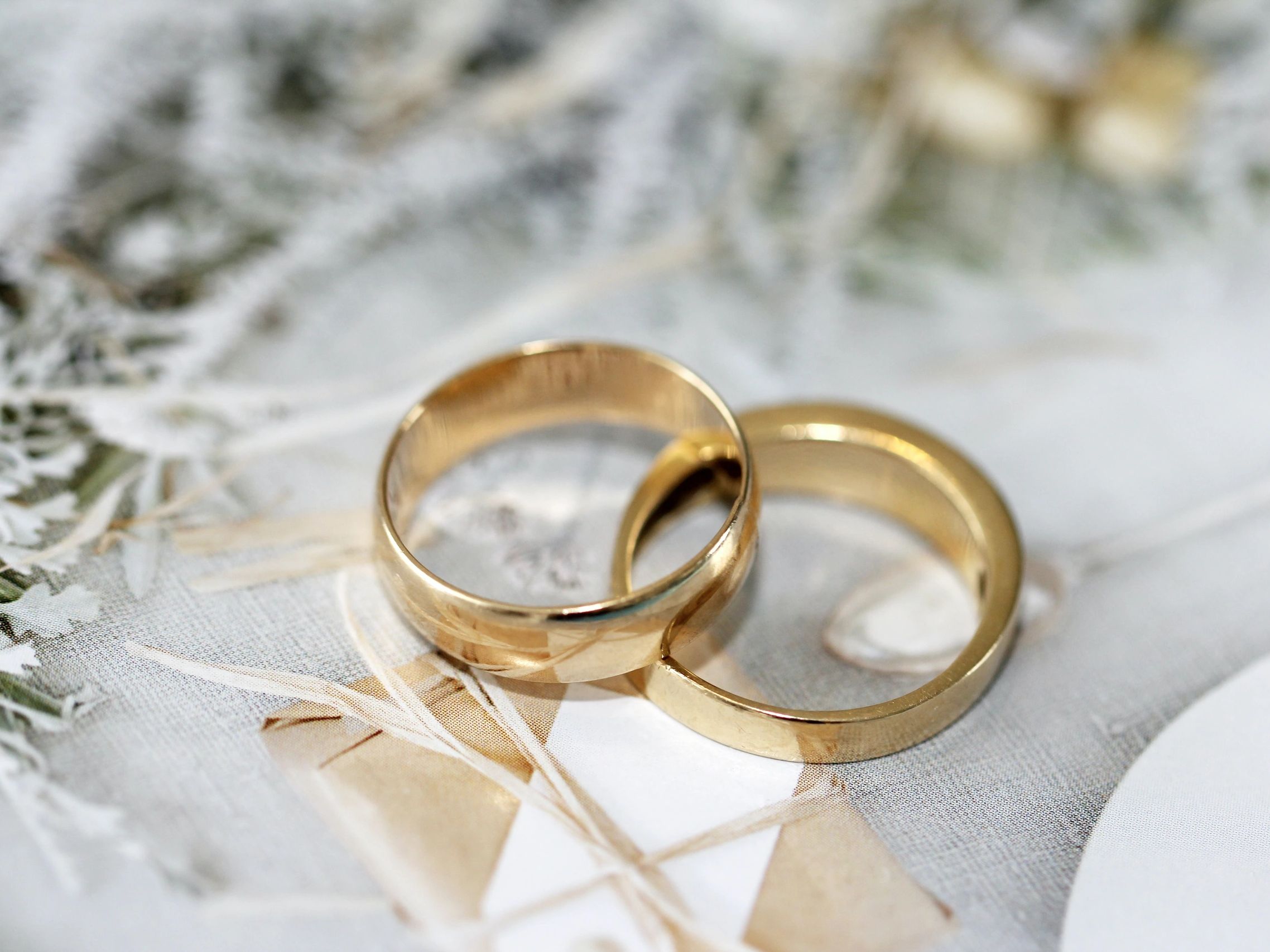 Two gold wedding rings on a delicate patterned fabric.