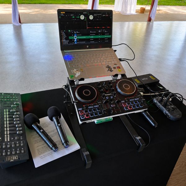 DJ setup with laptop, controller, microphones, and mixer on a table.