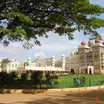 Majestic palace with domes and lush greenery under a large tree.