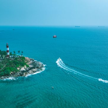 Lighthouse on rocky coast with boats in blue sea.