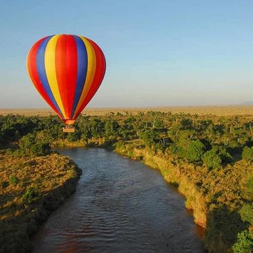 Colorful hot air balloon flying over a river and green forest landscape.