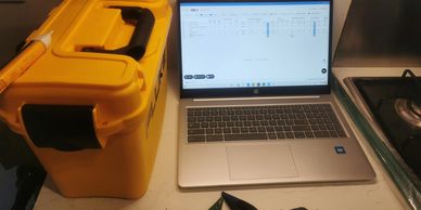 Yellow toolbox beside a laptop displaying a spreadsheet on a kitchen counter.