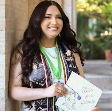Young graduate smiling with cap and honor cords outdoors.