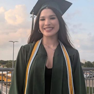 Young woman smiling in graduation gown and cap outdoors.