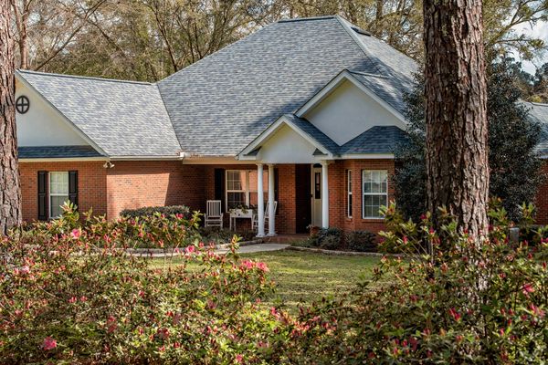 
The image displays a traditional brick house with a gray shingled roof and a covered porch.