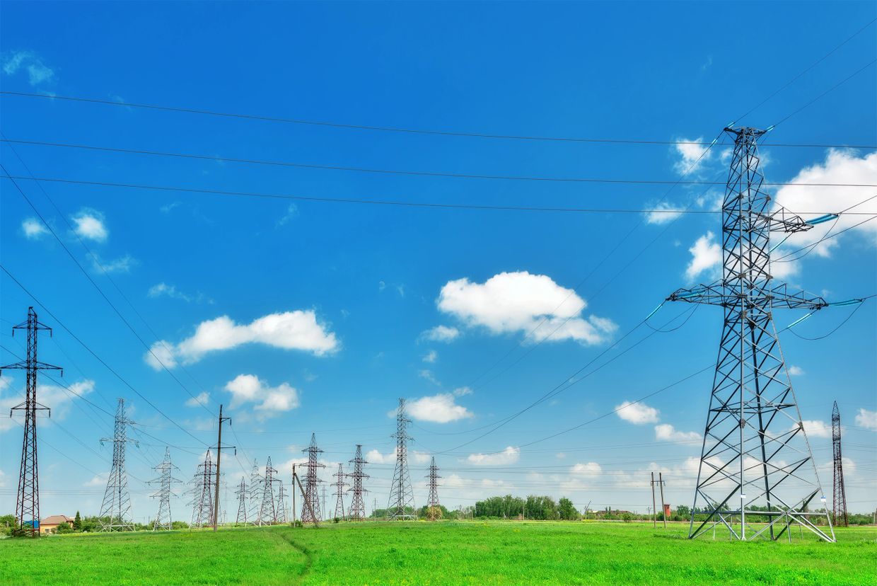 A field with multiple electrical transmission towers under a bright blue sky.