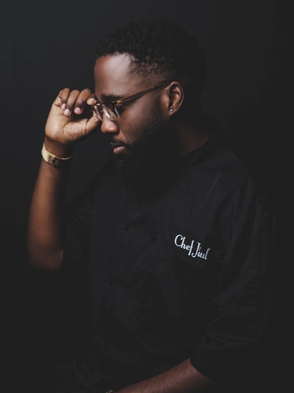 A thoughtful chef adjusting his glasses in a dark setting.