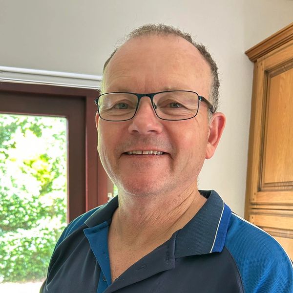 Smiling man wearing glasses and a blue polo shirt indoors near a window.