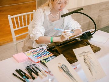 Artist carefully painting fashion designs at a well-organized workspace.