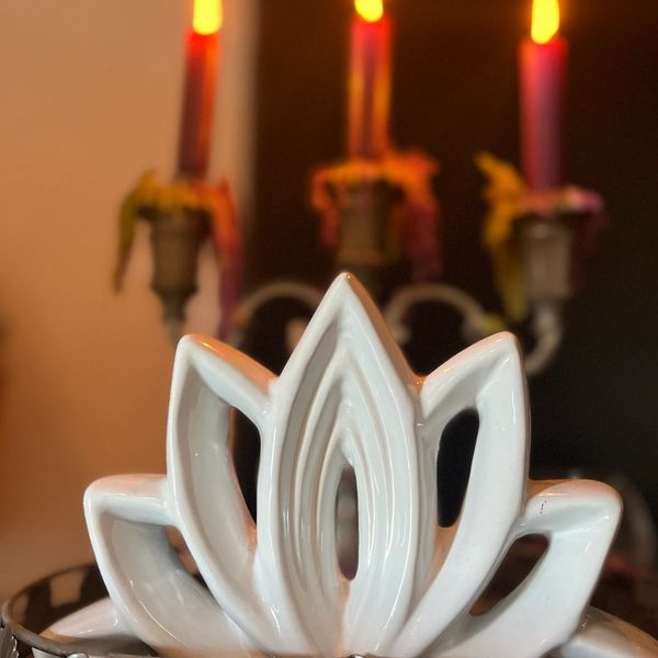 White ceramic lotus sculpture with three lit candles in the background.