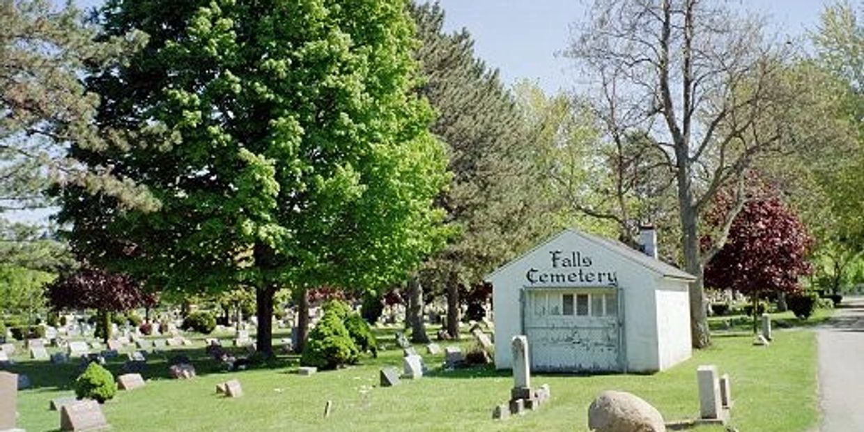 Scenic view of Falls Cemetery with lush trees and gravestones under a clear sky.