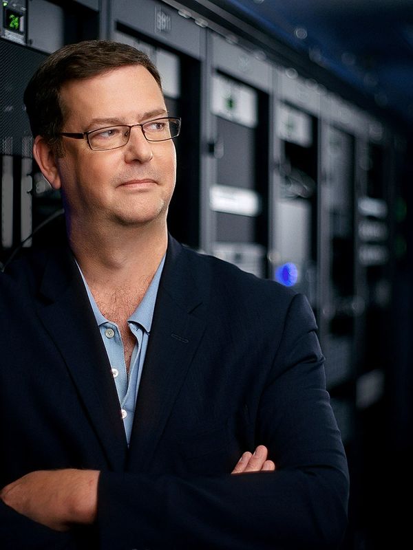 Man in glasses and blazer standing confidently in a server room.