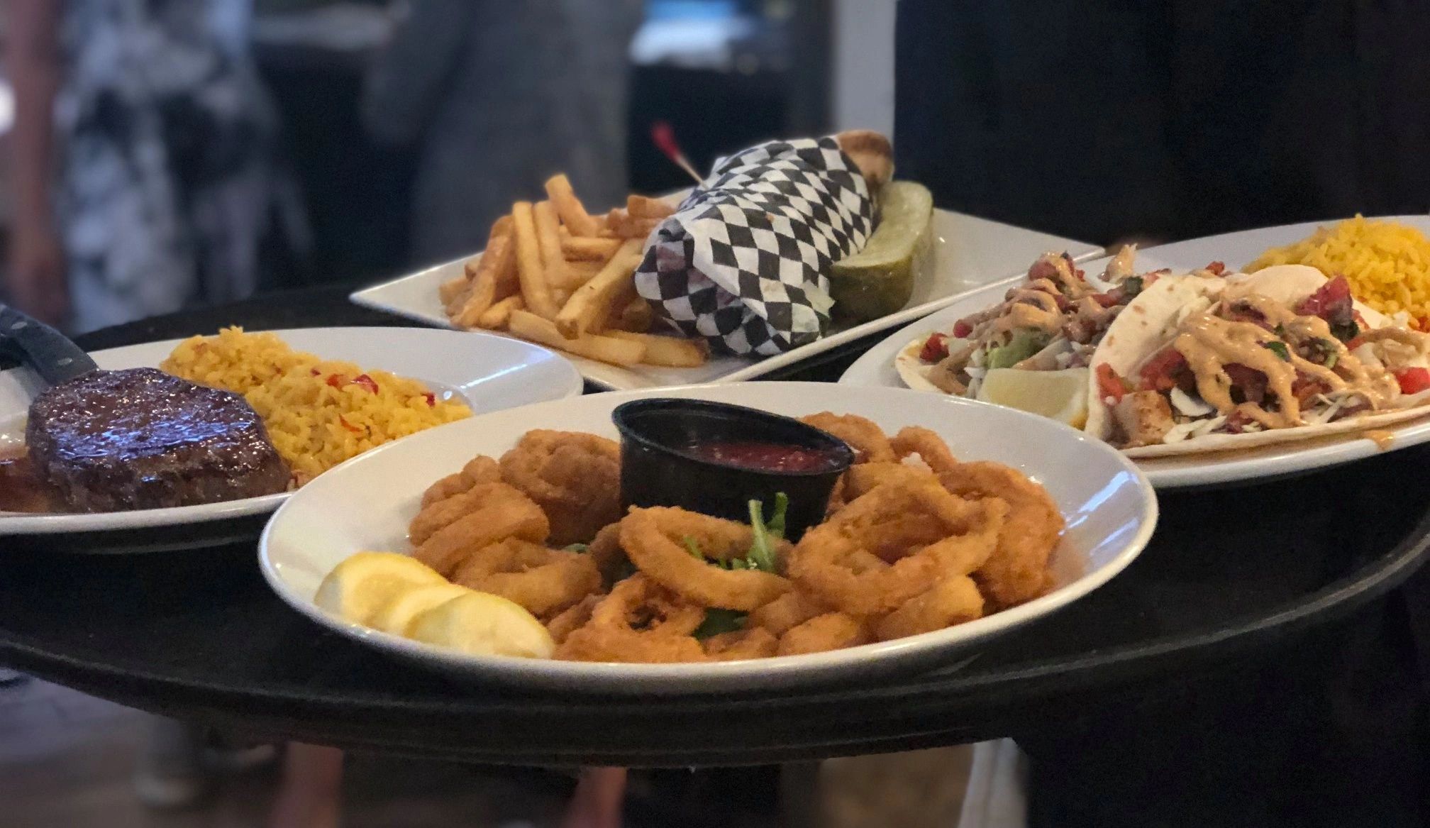 A table with fried calamari, fries, steak, rice, and tacos.