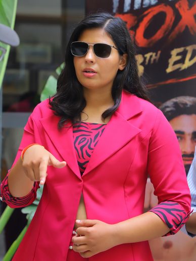 Woman in pink blazer and sunglasses gesturing.
