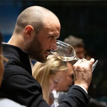 Man intently smelling wine in a glass at a tasting event.
