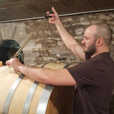 Man extracting liquid from a wooden barrel in a cellar.