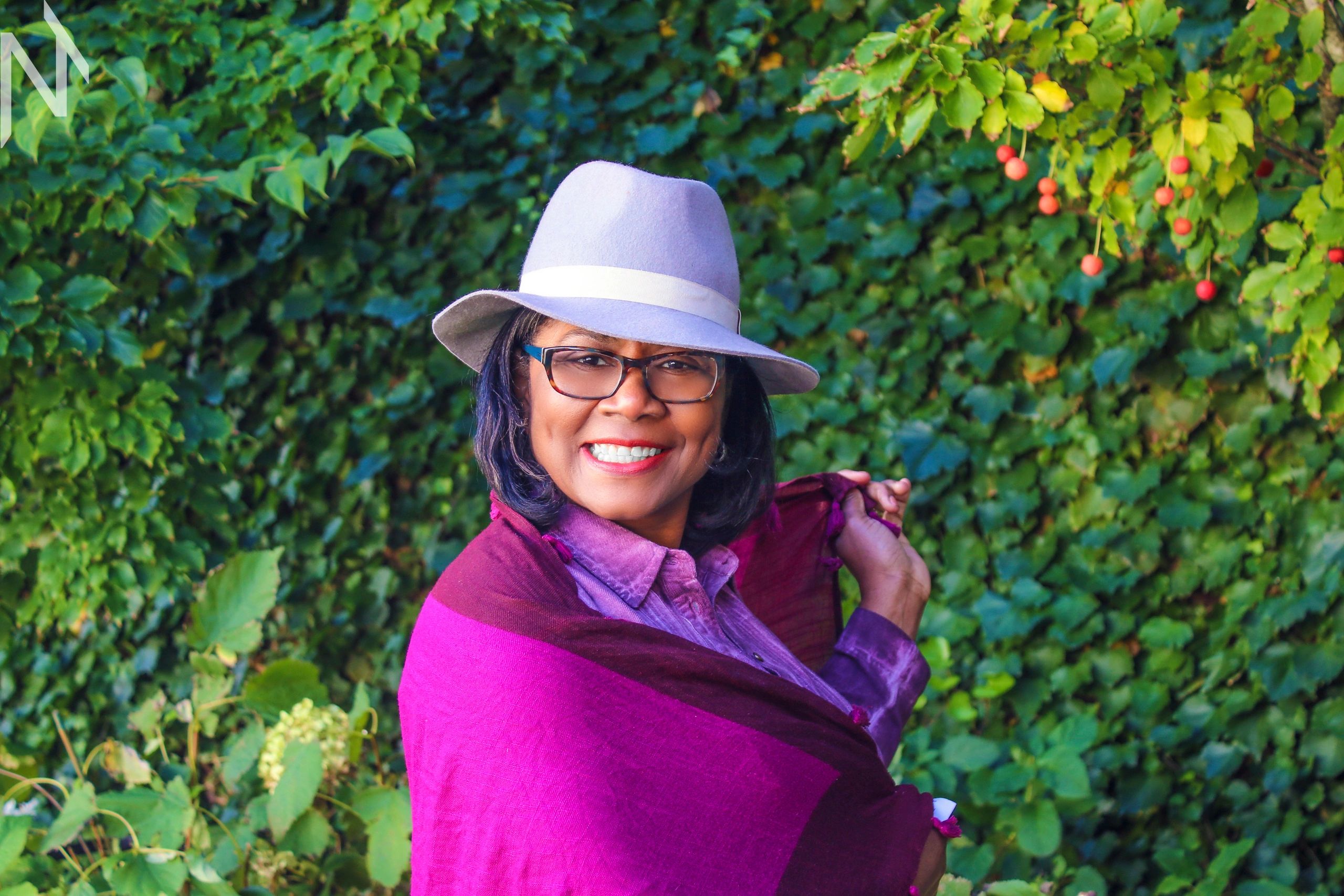 A woman wearing a hat and glasses looks at the camera,