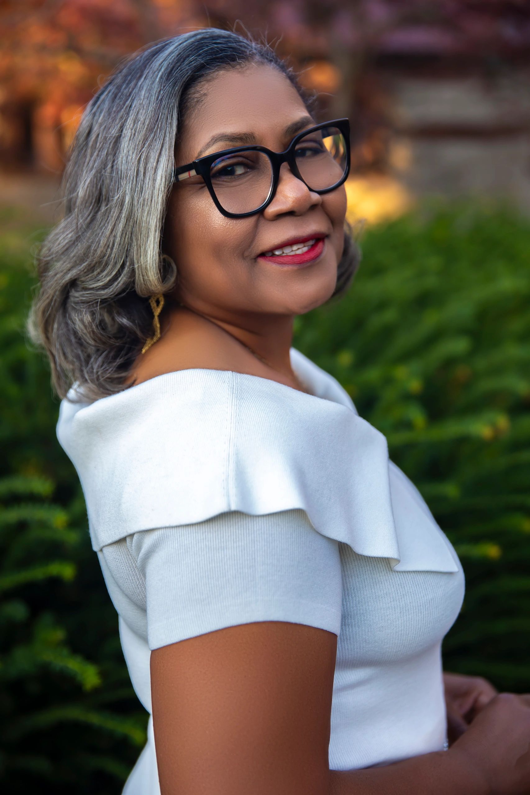 a woman in a white suit and glasses looks at the camera