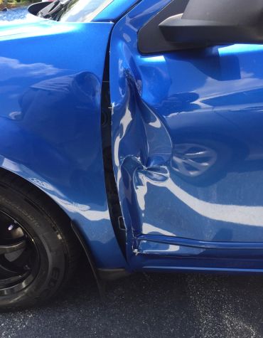 Blue car with a large dent on the side door.