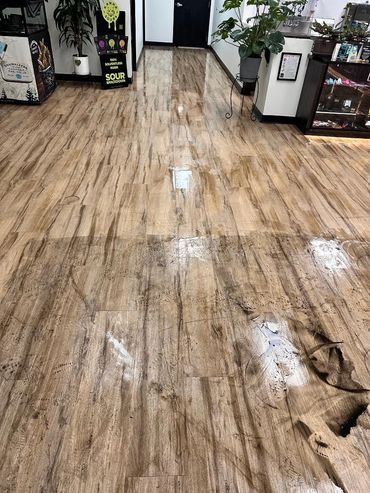 Damaged wooden floor with peeling and warping near the corner of a room.