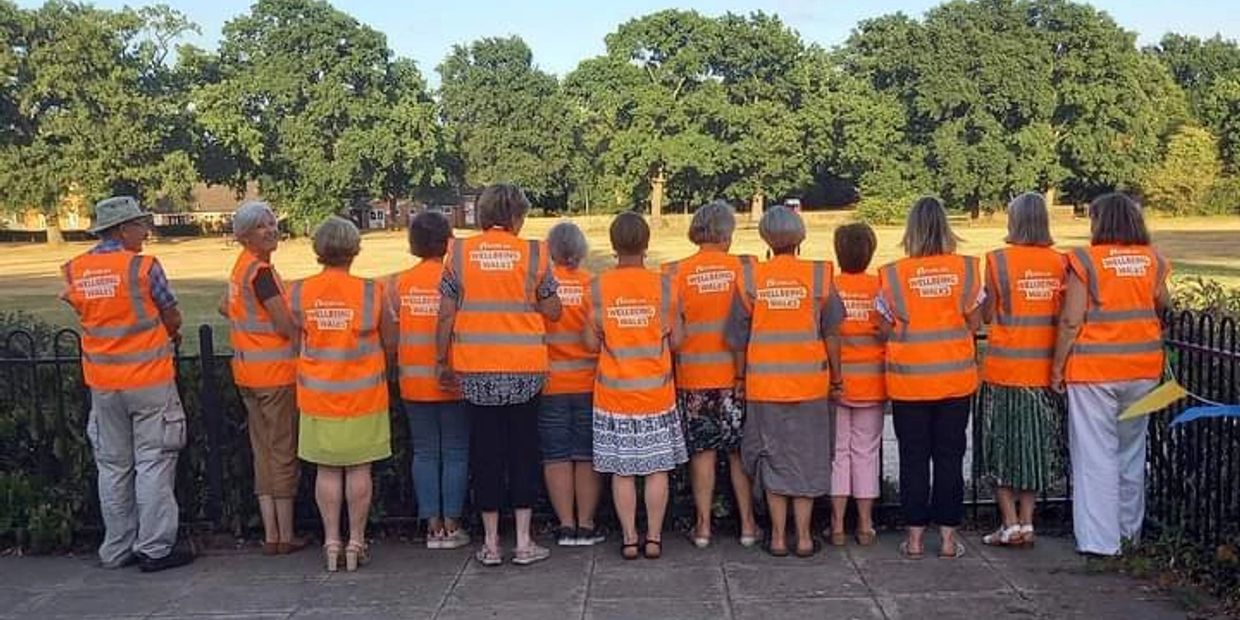 A group of people wearing orange safety vests facing away in a park.