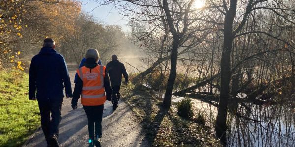 People walking along a misty riverside path on a sunny day.
