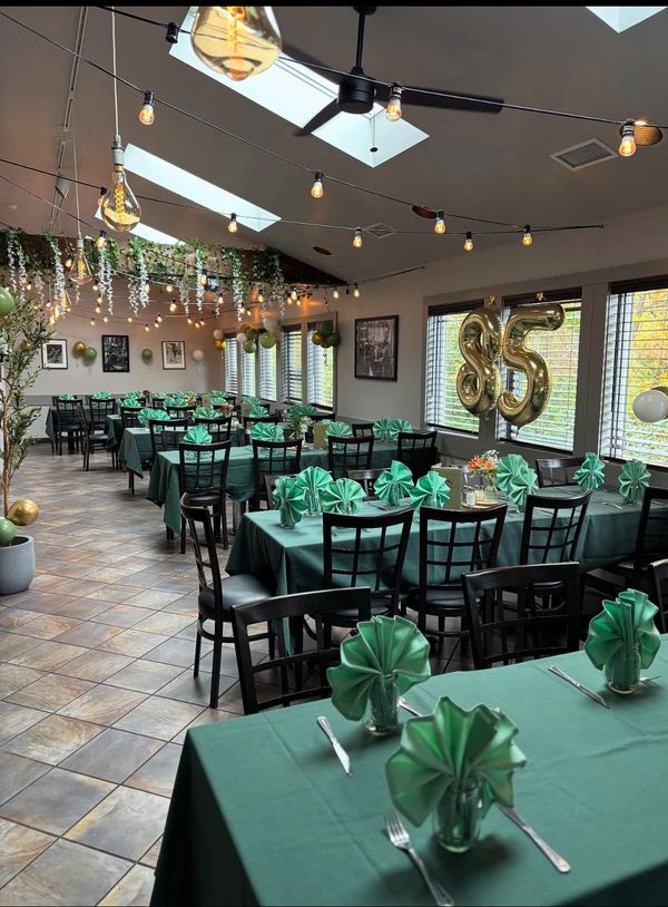 Elegant dining area decorated for a 25th celebration with green tablecloths and gold balloons.