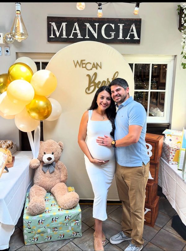 Couple celebrating pregnancy at a decorated baby shower with balloons and a teddy bear.