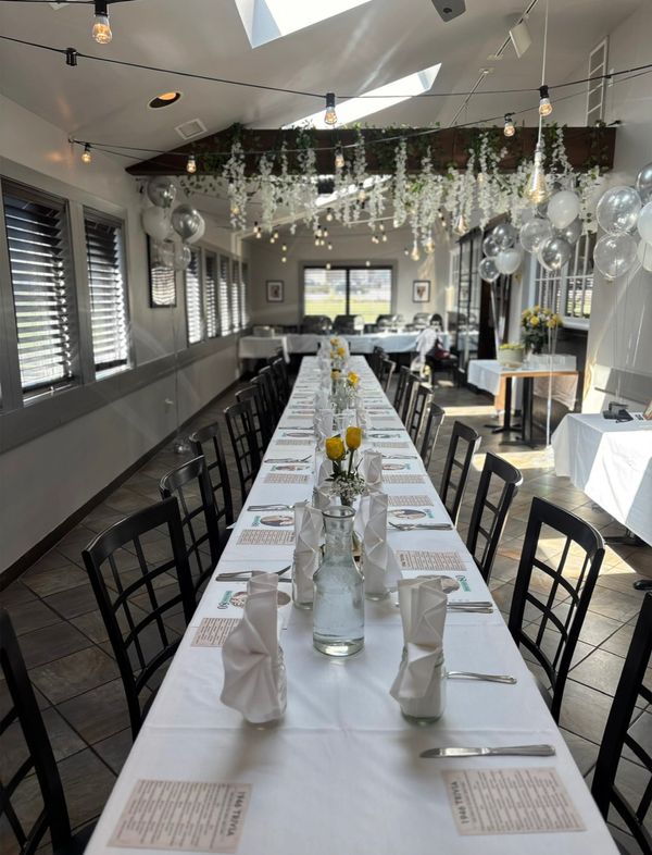 Long dining table set with white linens and yellow flowers in a decorated room.
