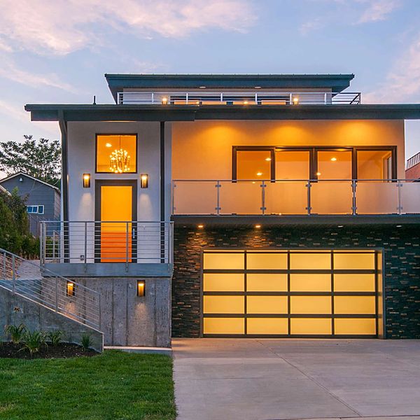 Modern house with warm lighting and glass garage door at dusk.