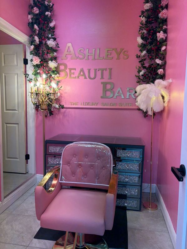 Pink and gold styling chair beneath Ashley’s Beauti Bar signage, surrounded by floral decorations in the Miami Gardens salon suite.